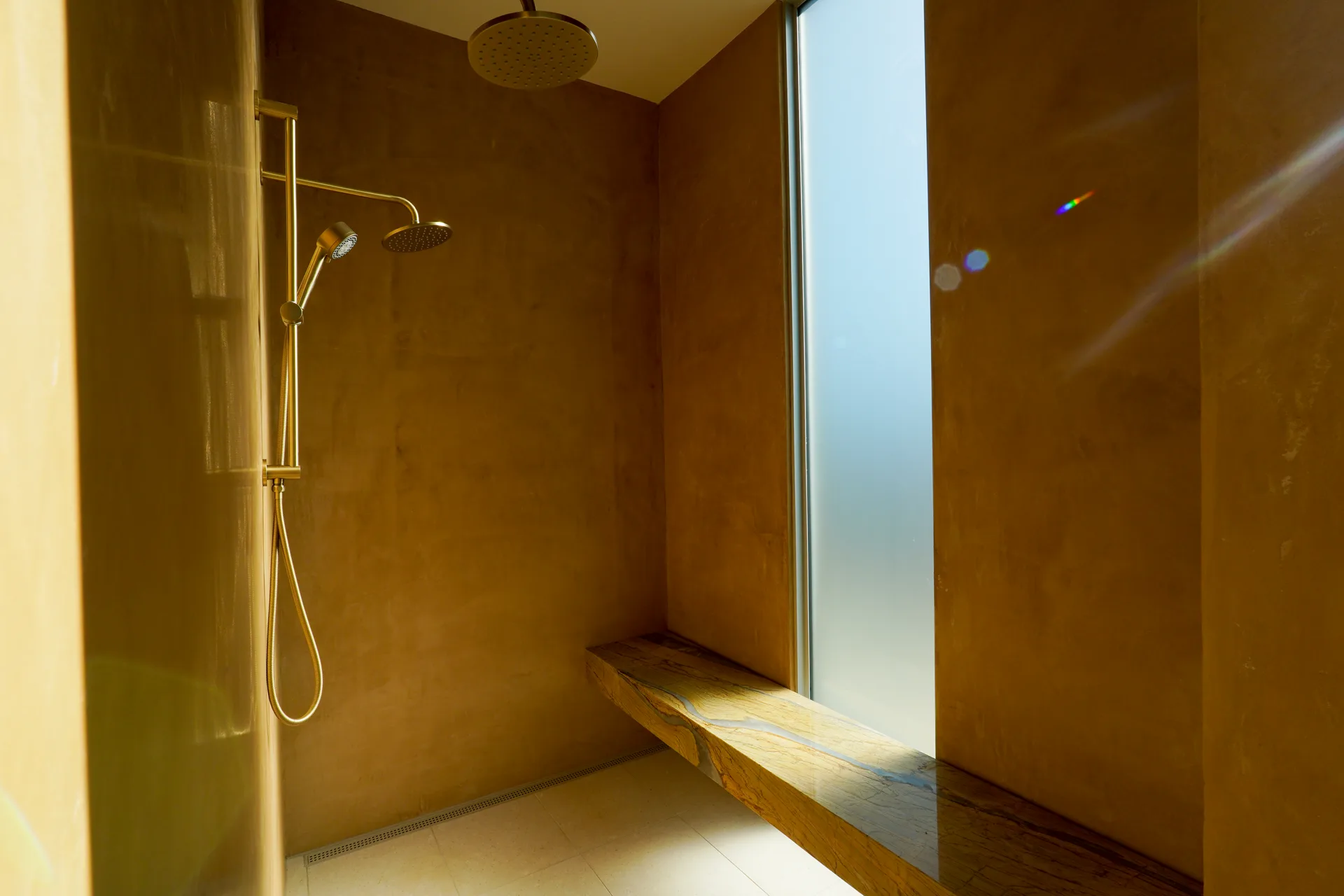 Primary shower bench in natural stone below a frosted window