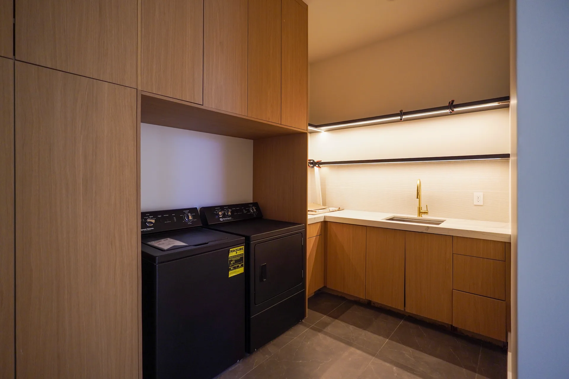 Laundry room with oak cabinetry and lit open shelving